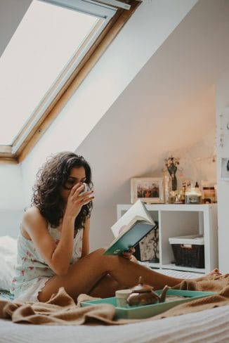 Γυναίκα καθισμένη στο κρεβάτι διαβάζει βιβλίο και πίνει τσάι.