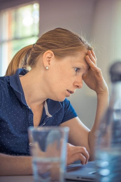 Νεαρή γυναίκα μπροστά από τον υπολογιστή που κρατάει το κεφάλι της με το χέρι της και φαίνεται μπερδεμένη.