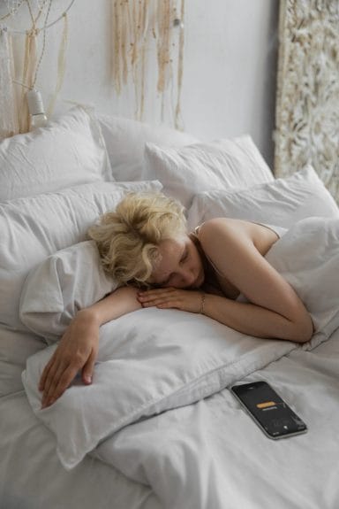 Γυναίκα κοιμάται και έχει το κινητό δίπλα της στο κρεβάτι με ανοιγμένη κάποια από τις εφαρμογές του.