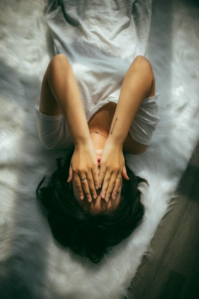 Γυναίκα ξαπλωμένη στο κρεβάτι κρύβει το πρόσωπό της με τα χέρια της