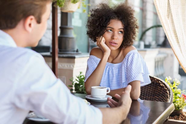 Γυναίκα με βαριεστημένη έκφραση καθισμένη σε καφετέρια μαζί με έναν άνδρα που της μιλά
