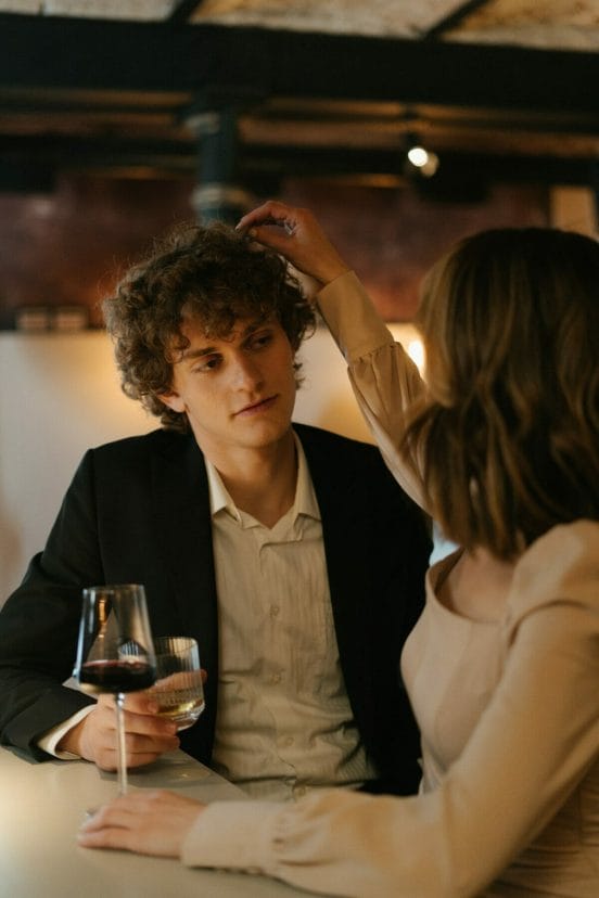 Γυναίκα απαλά αγγίζει τα μαλλιά του άνδρα που κάθεται δίπλα της στο μπαρ