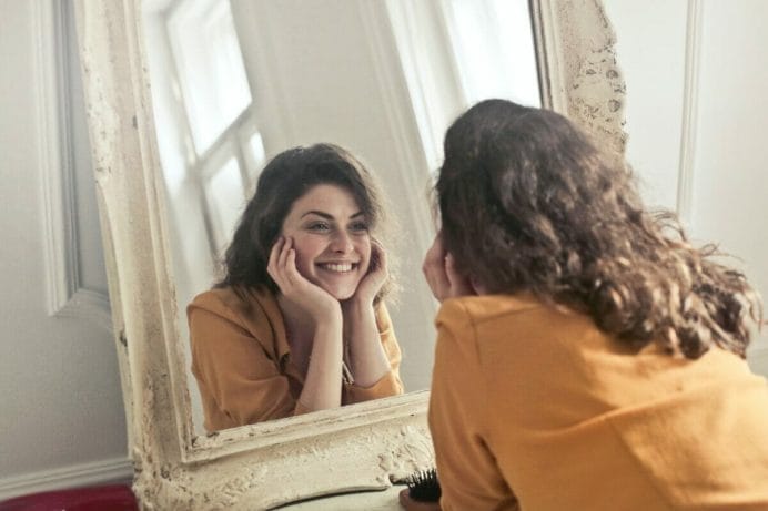 Γυναίκα κοιτάζει χαρούμενη τον εαυτό της στον καθρέφτη