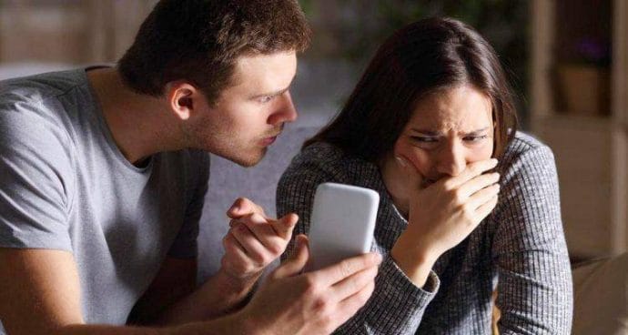 Χειριστικός σύντροφος δείχνει την οθόνη του κινητού στη σύντροφό του η οποία είναι στεναχωρημένη 